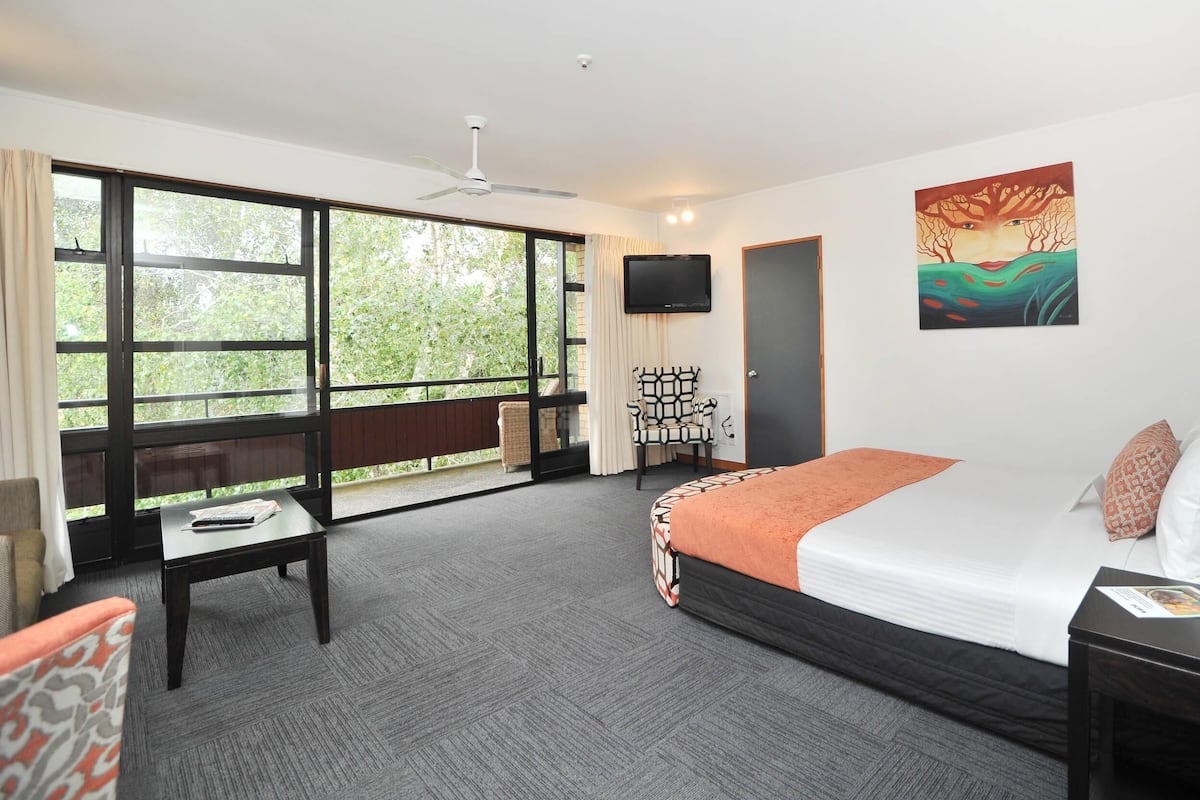 A hotel room with a large window, a bed, a desk, and a chair.
