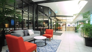 Um lobby com sofá, cadeiras, mesa de centro e plantas em vasos.