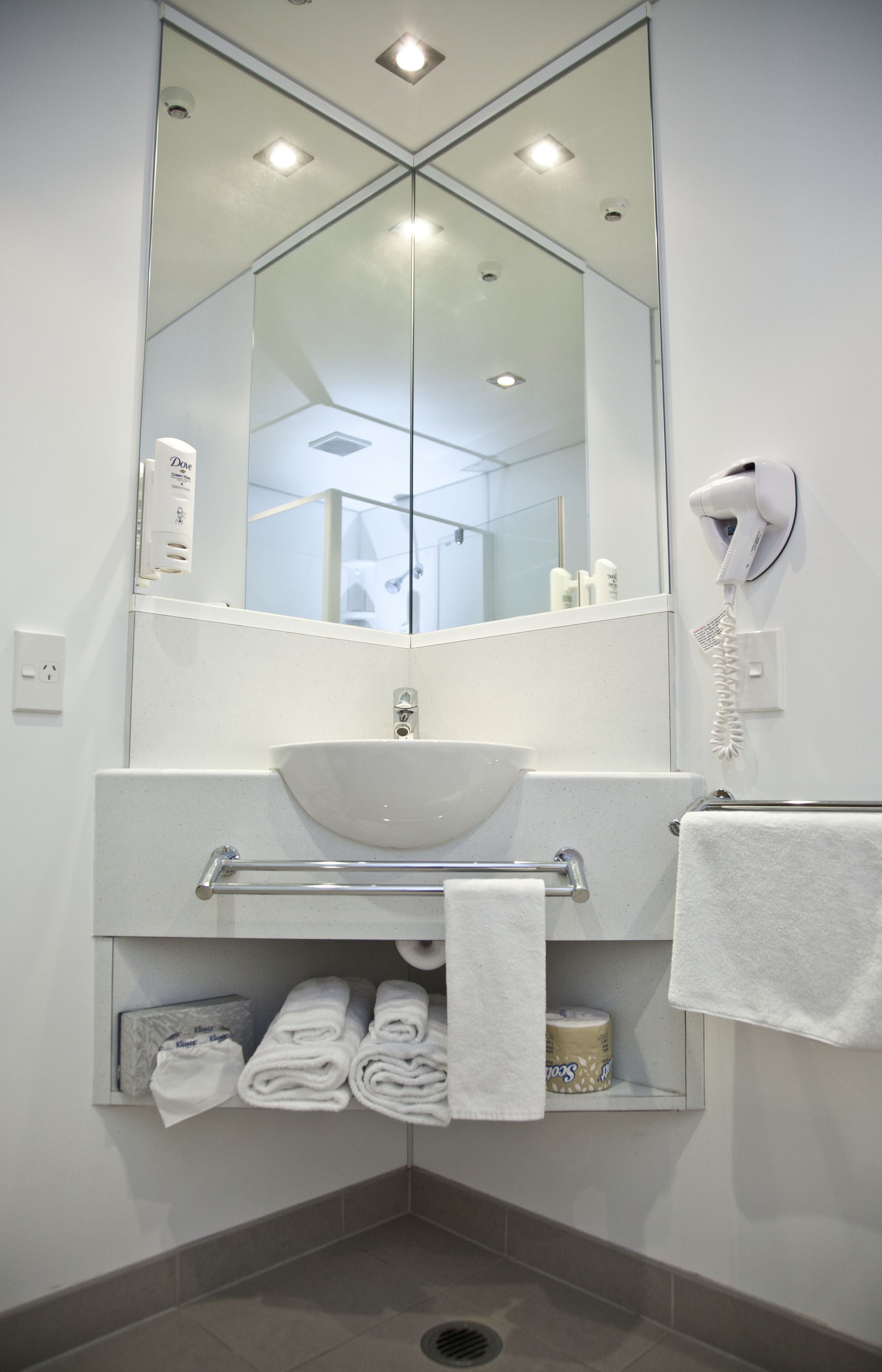 Un baño moderno con un espejo grande, lavamanos blanco, toallero y secador de pelo.