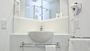 A modern bathroom with a large mirror, white sink, towel rack, and a hair dryer.