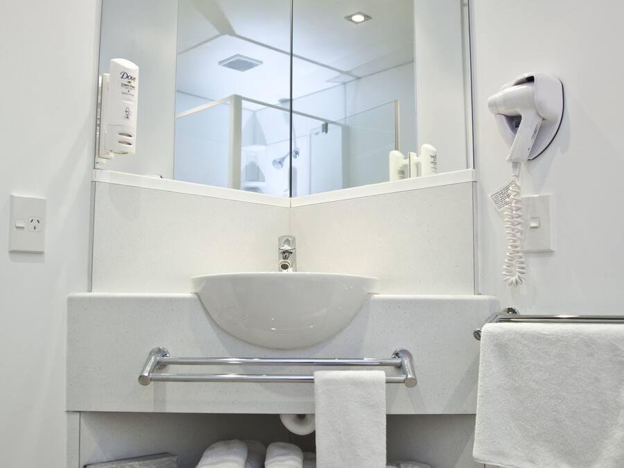 A modern bathroom with a large mirror, white sink, towel rack, and a hair dryer.