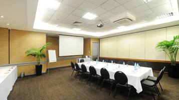 A conference room with a long table, chairs, a projector screen, and two potted plants.