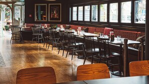 Interior de restaurante com chão de madeira, cadeiras e mesas pretas, e parede vermelha estampada.
