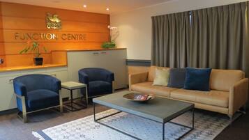 Una sala de estar moderna con un sofá, dos sillones, una mesa de centro y un mostrador de recepción con un cartel que dice 'FUNCTION CENTRE'.
