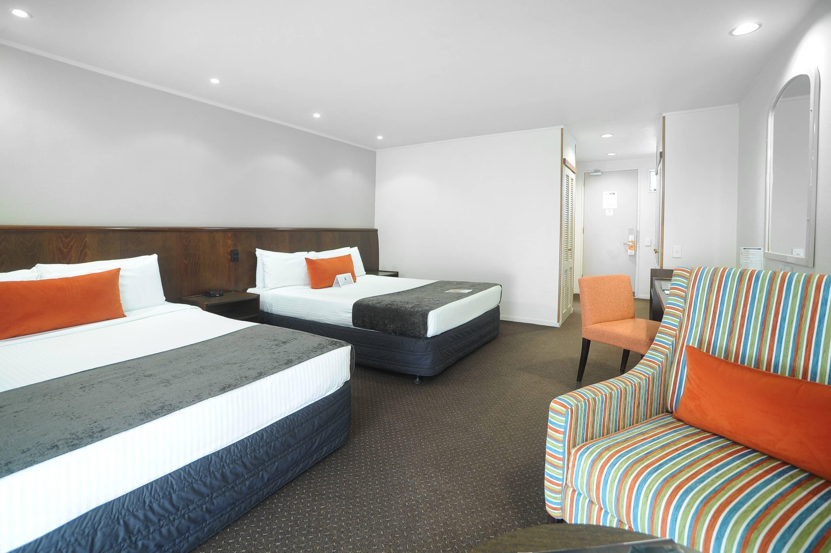Una habitación de hotel con dos camas, un sillón a rayas y una mesita.