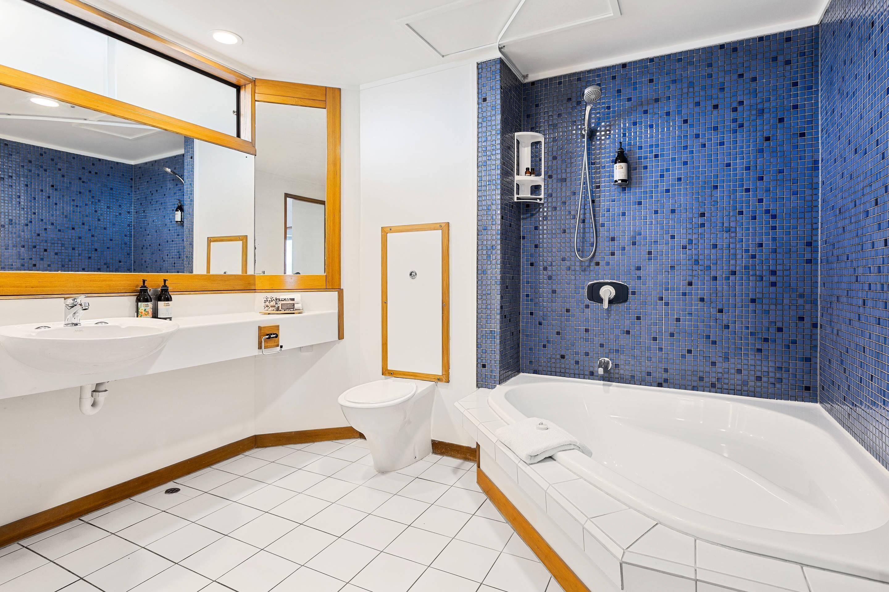 A bathroom with a white sink, toilet, and bathtub, blue mosaic tiles, and a mirror with a wooden frame.