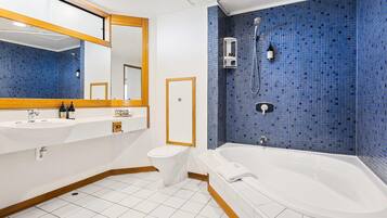 A bathroom with a white sink, toilet, and bathtub, blue mosaic tiles, and a mirror with a wooden frame.