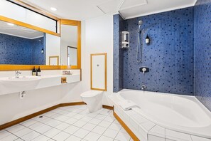 A bathroom with a white sink, toilet, and bathtub, blue mosaic tiles, and a mirror with a wooden frame. - Quality Hotel Lincoln Green (Auckland)