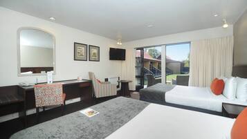 Habitación de hotel con escritorio, dos camas, una silla, televisor y vistas al exterior.