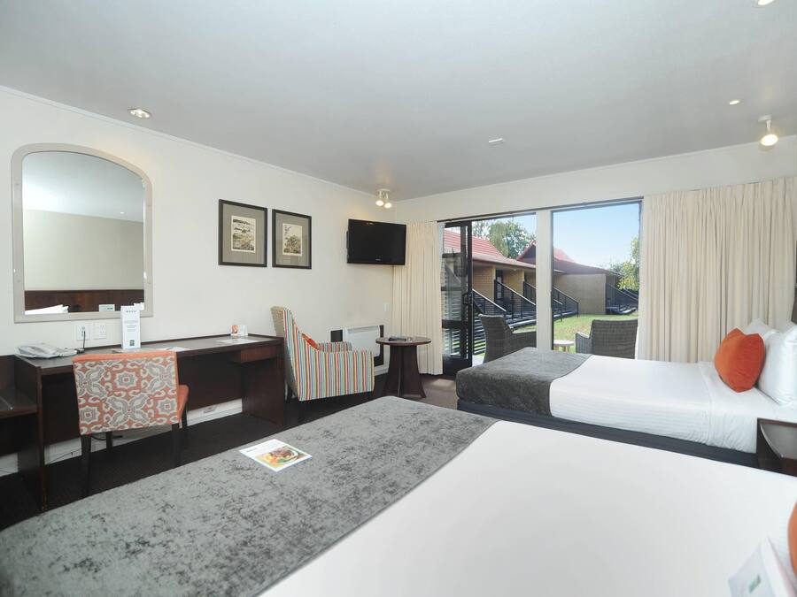 Habitación de hotel con escritorio, dos camas, una silla, televisor y vistas al exterior.