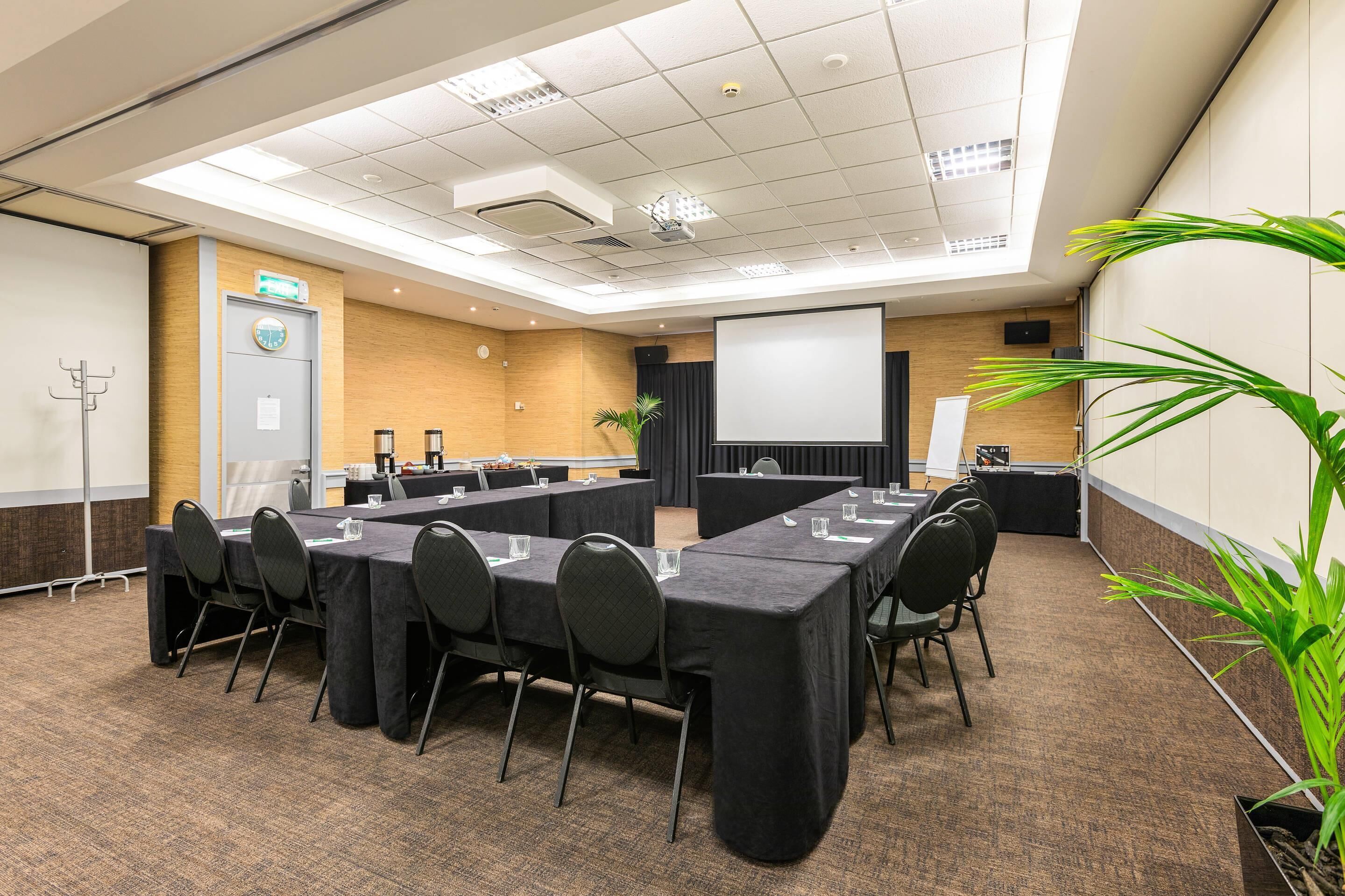 A conference room with tables, chairs, a projector screen, and a plant.