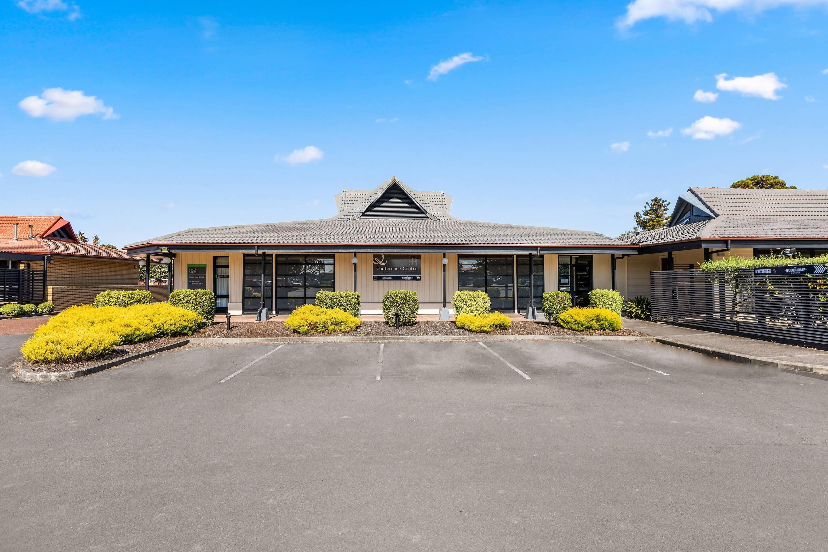 A building with a flat roof, a central entrance, and a parking lot in front.