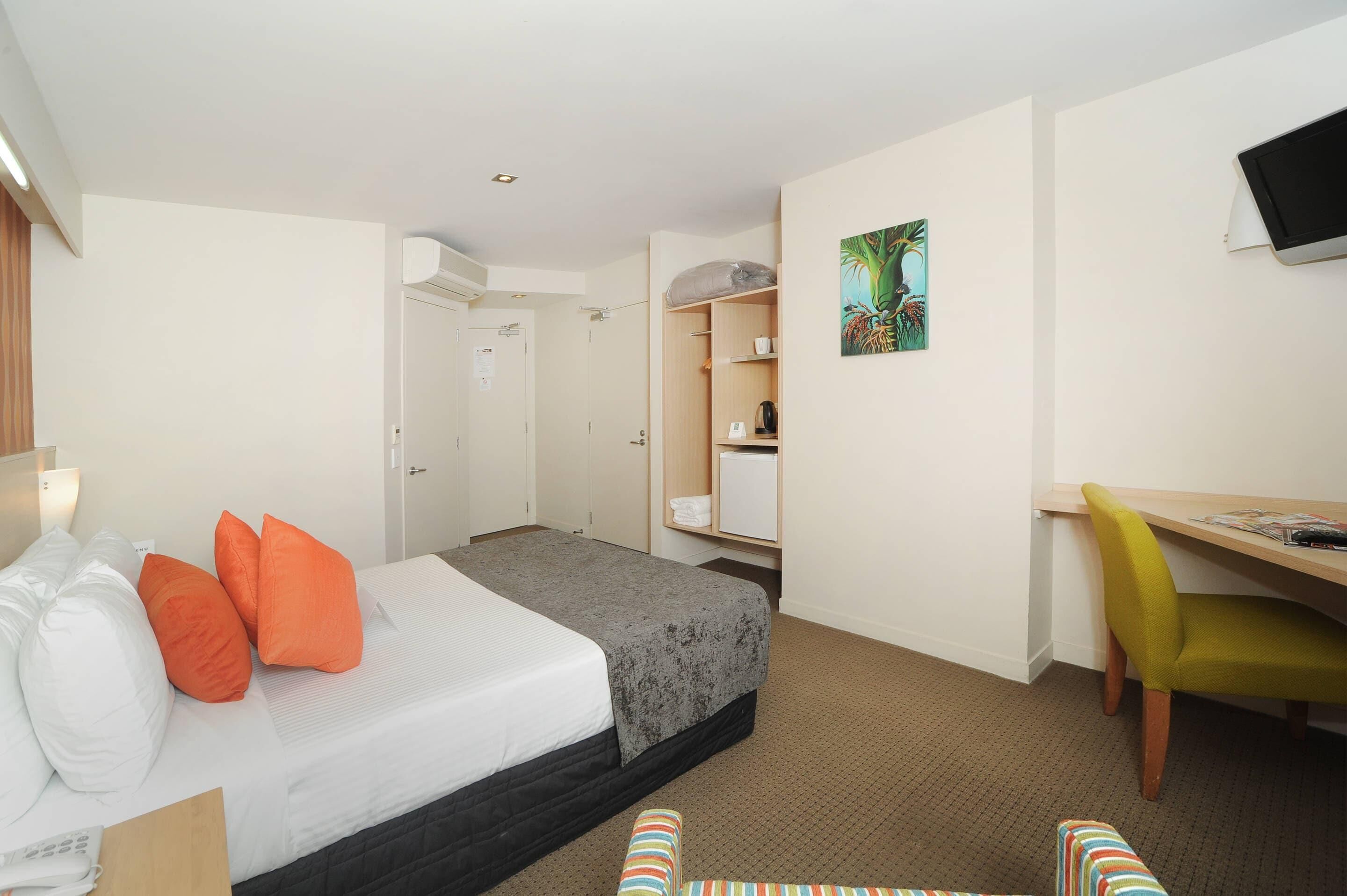 A hotel room with a bed, a desk, a chair, a television, and a wardrobe.