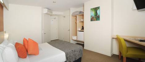 A hotel room with a bed, a desk, a chair, a television, and a wardrobe.