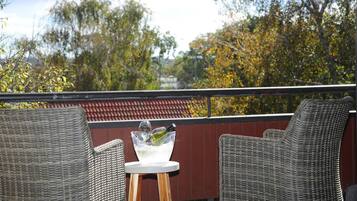 Une chaise et une table en osier, avec un saladier en verre contenant une bouteille et des glaçons, sur un balcon.