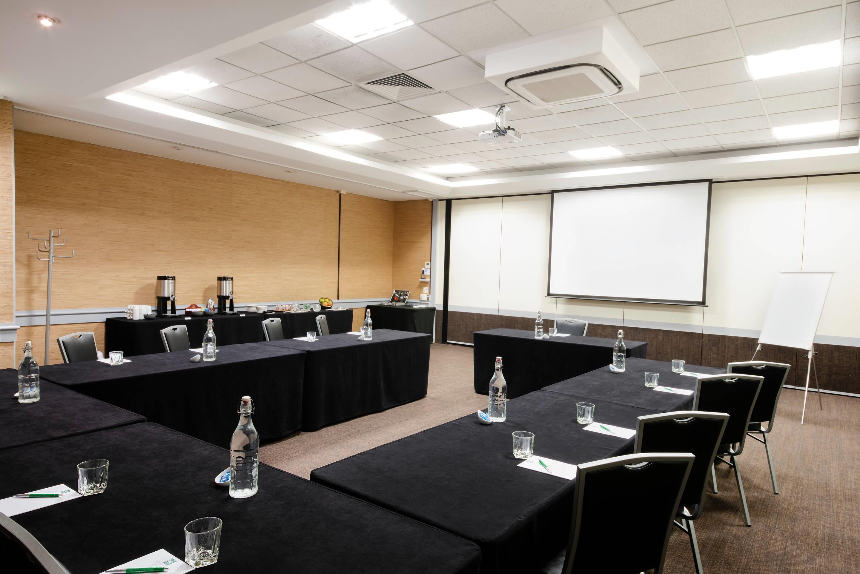 Ein Konferenzraum mit Tischen, Stühlen, einer Projektionsleinwand und einer Whiteboard-Tafel.