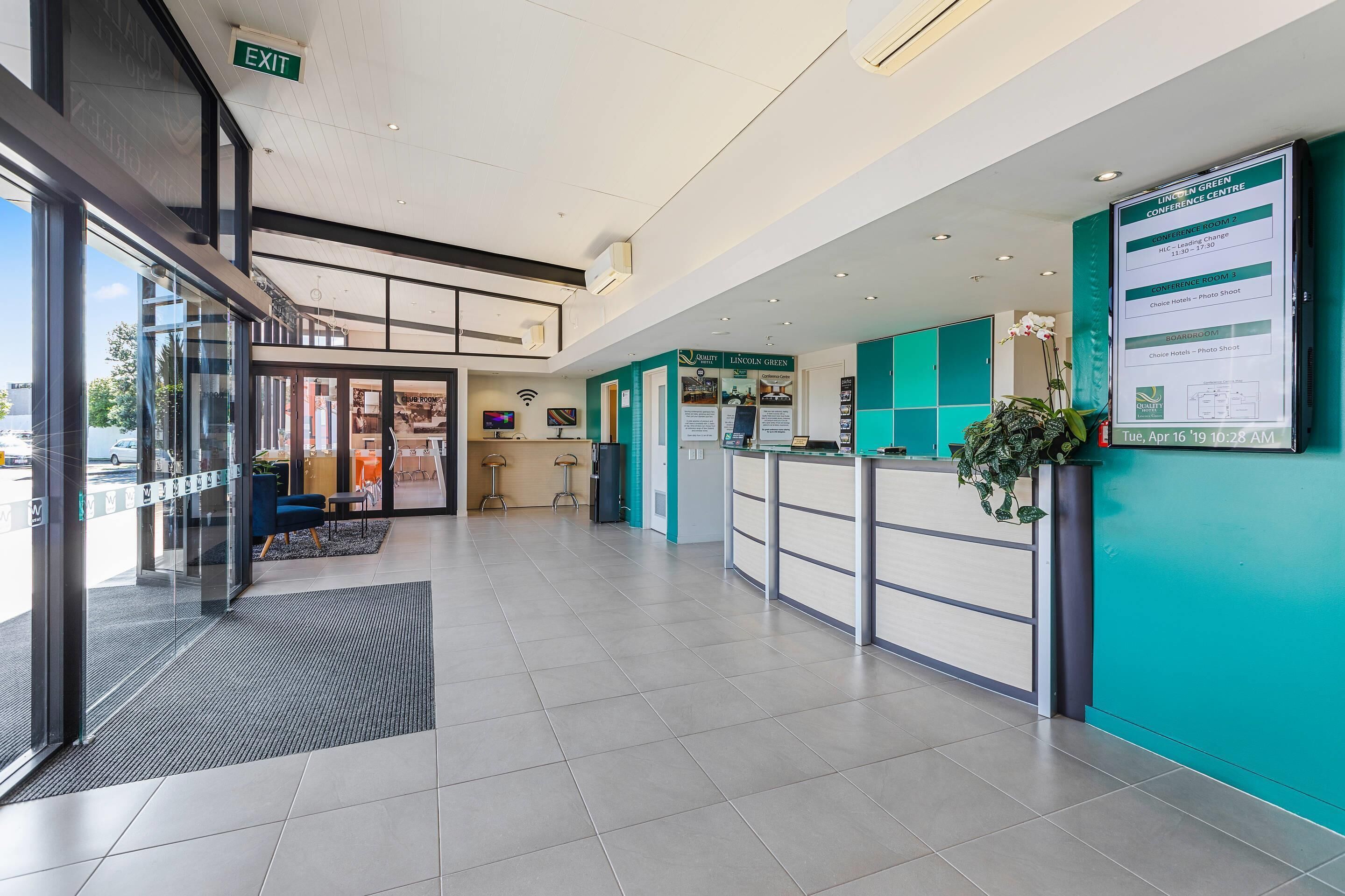 Een hotel receptiegebied met een glazen ingang, een receptiebalie, een zithoek en een bord met daarop 'conferentiecentrum'.