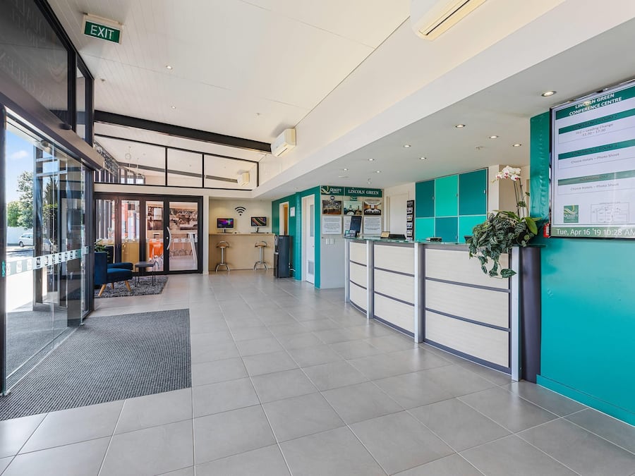 Een hotel receptiegebied met een glazen ingang, een receptiebalie, een zithoek en een bord met daarop 'conferentiecentrum'.