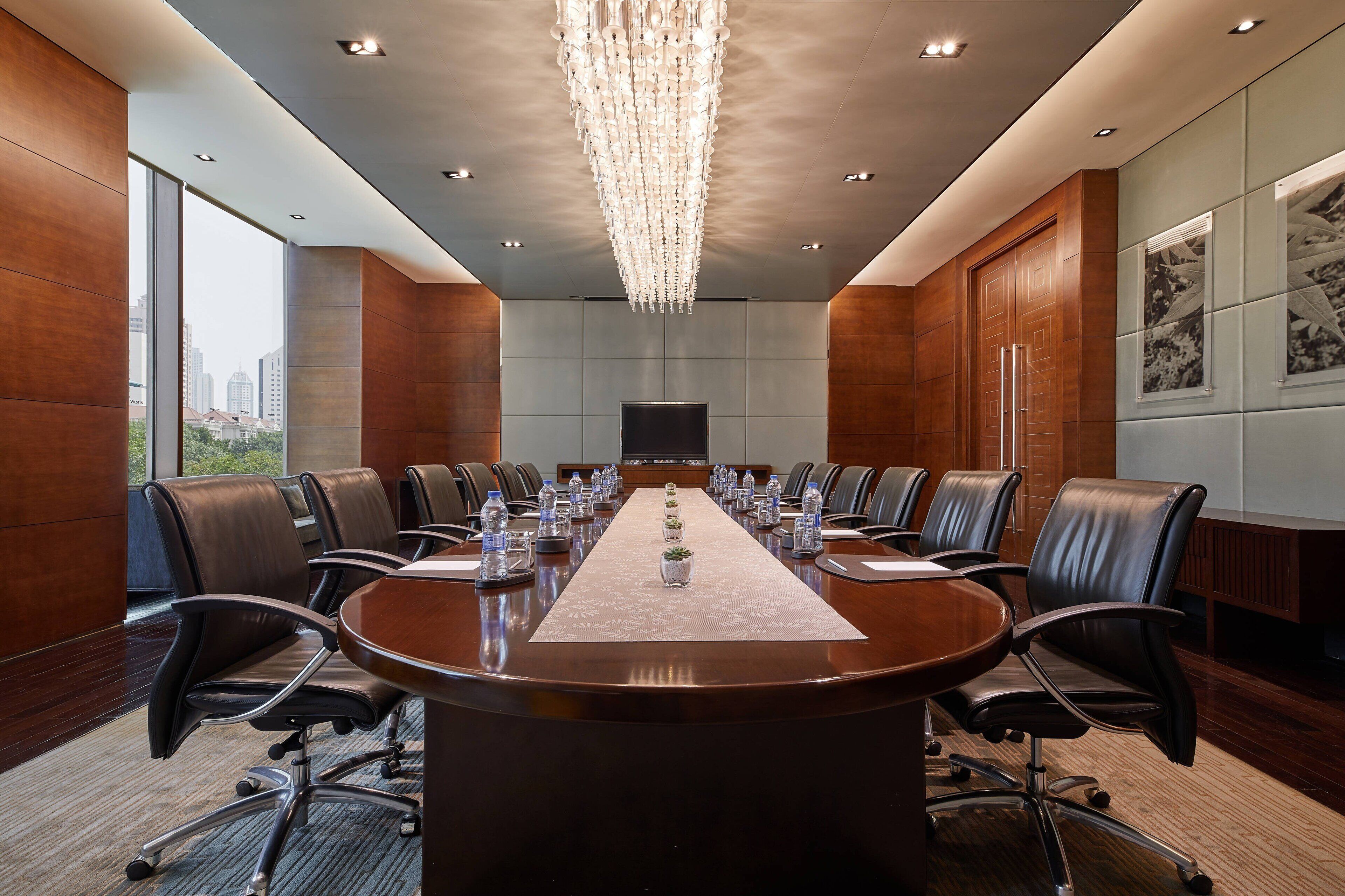 A conference room with a long table, leather chairs, and a chandelier.
