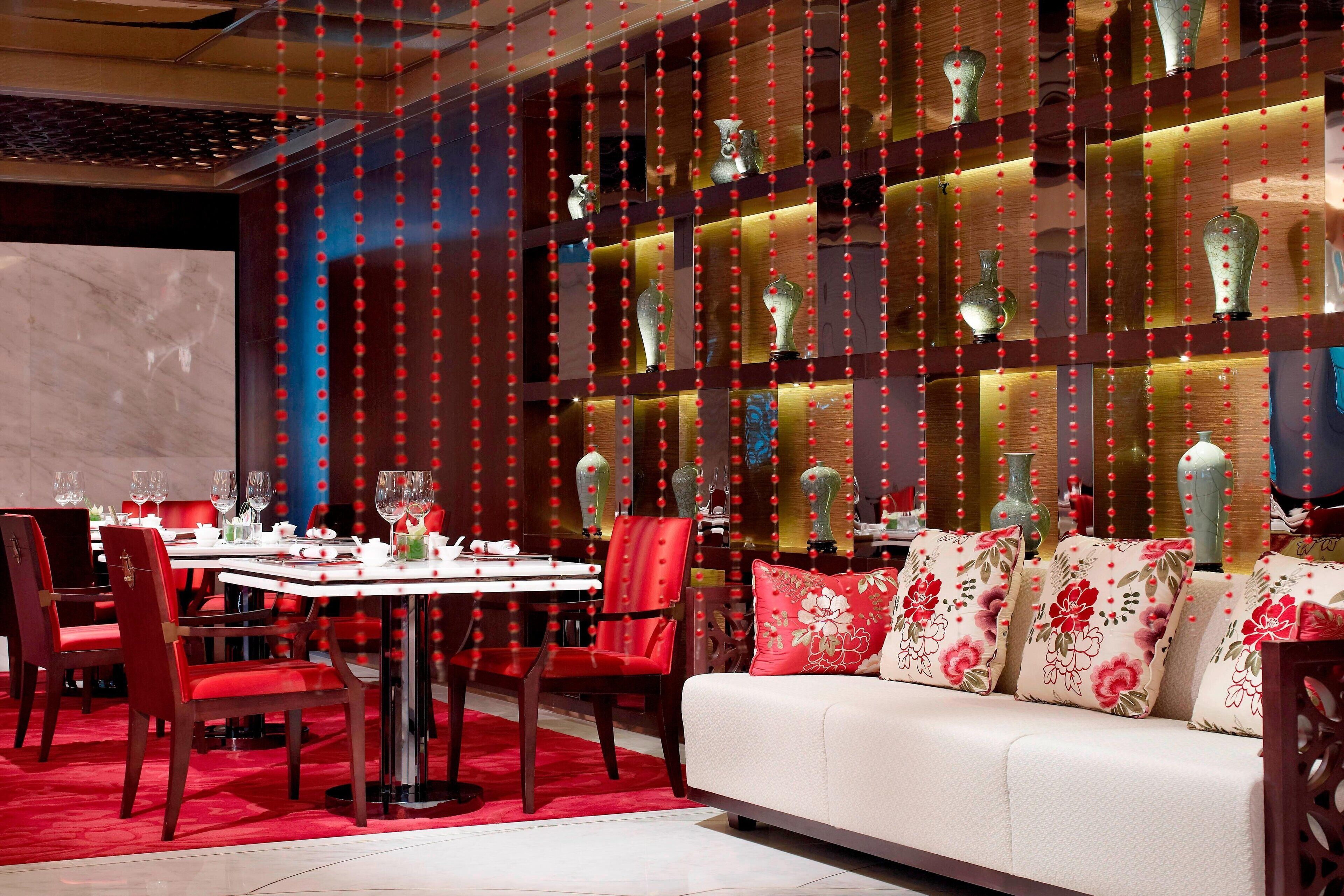 A dining area with a round table, red chairs, and a sofa with floral cushions.