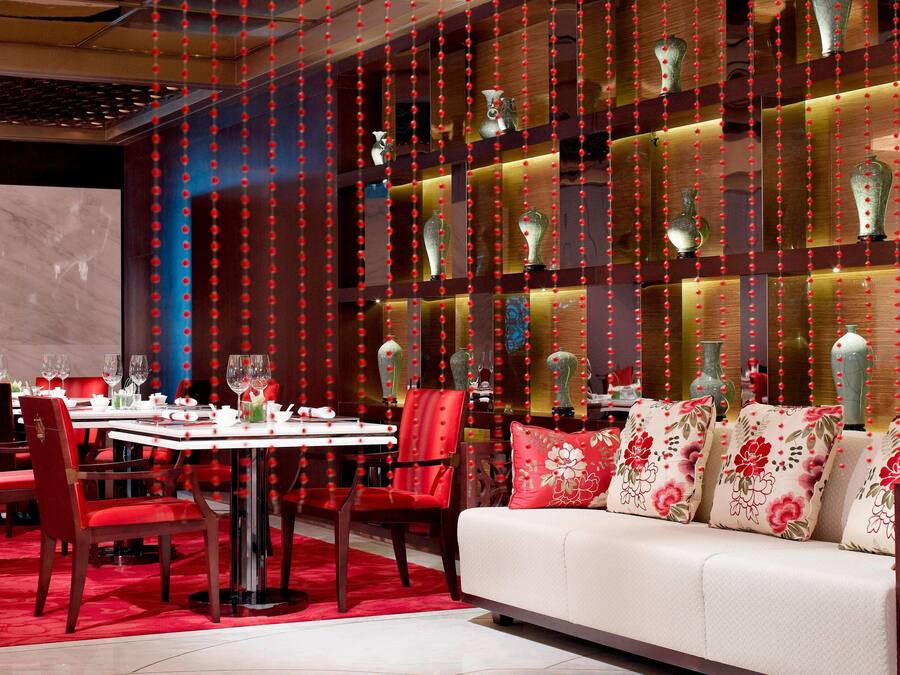 A dining area with a round table, red chairs, and a sofa with floral cushions.