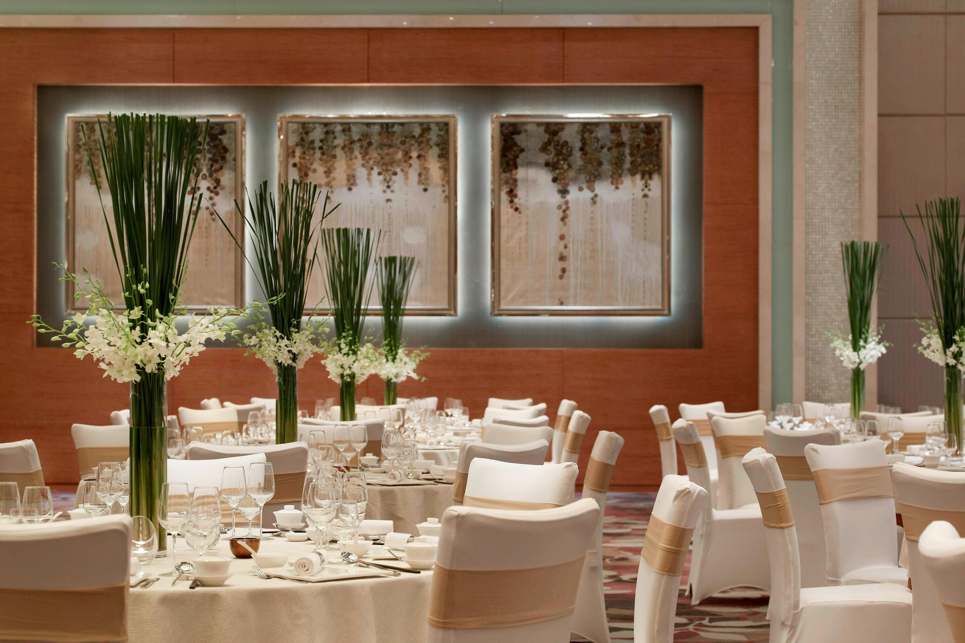 A banquet hall with round tables, white chairs, and floral centerpieces.