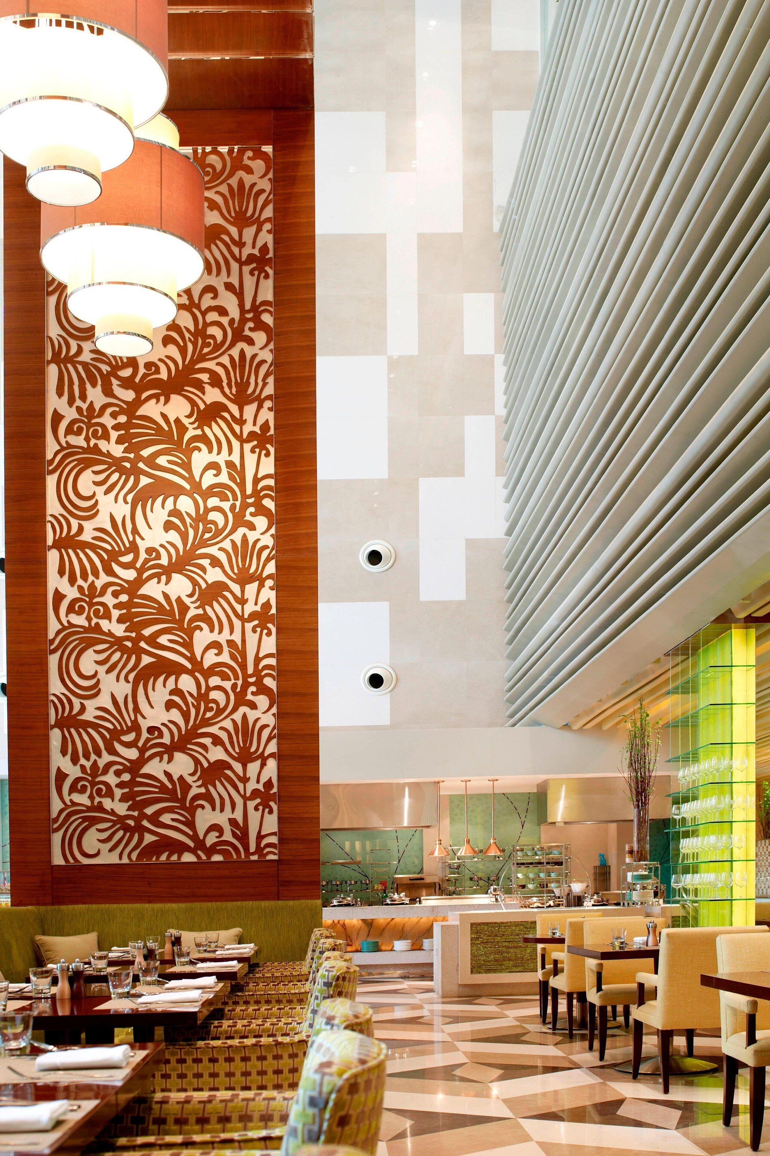 Un vestíbulo de hotel moderno con decoración de pared estampada, una zona de bar y un área de comedor con mesas y sillas.