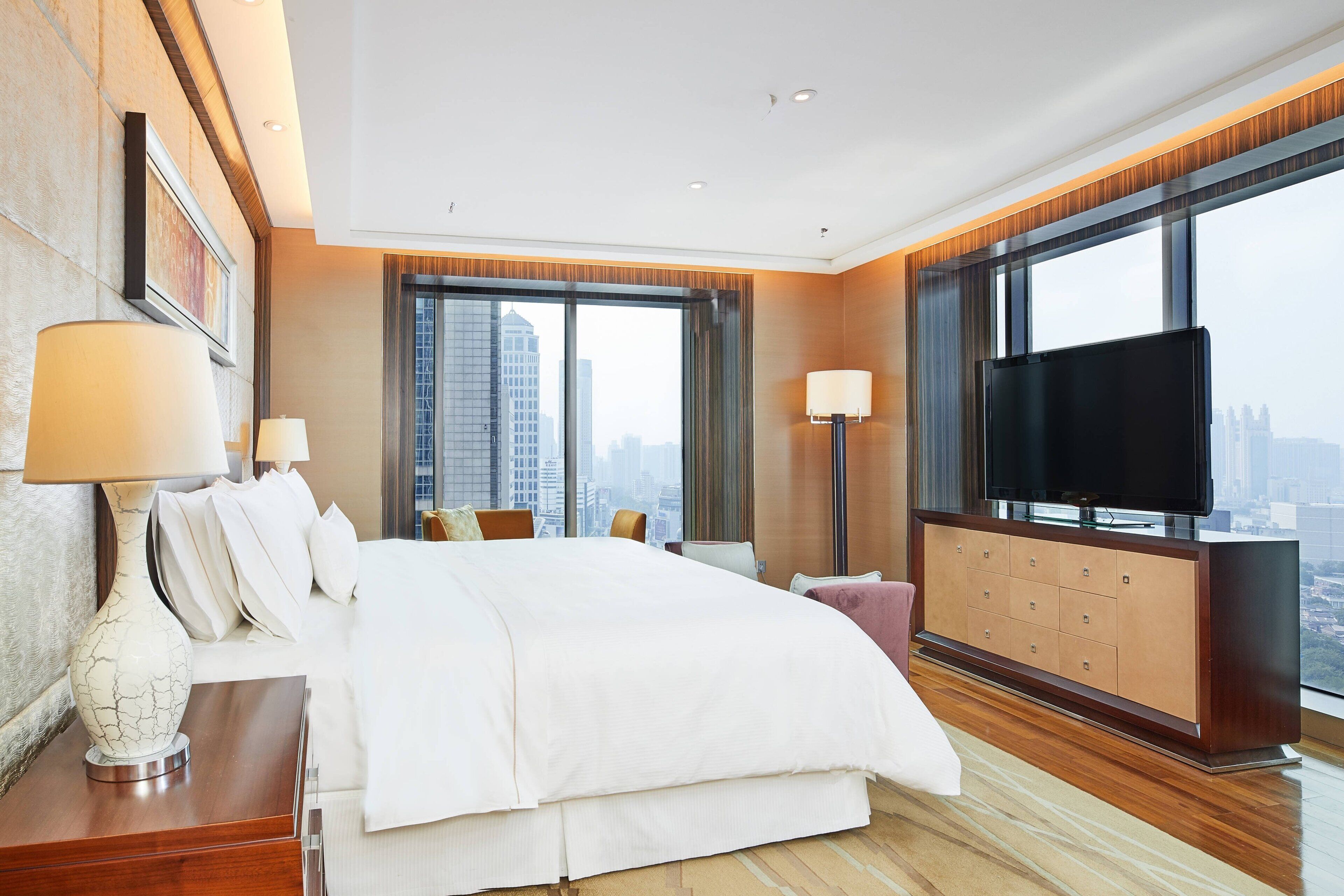 A modern hotel room with a large bed, a flat-screen TV, and a city view.