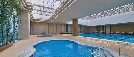 An indoor swimming pool with a skylight ceiling, lounge chairs, and a stone wall.
