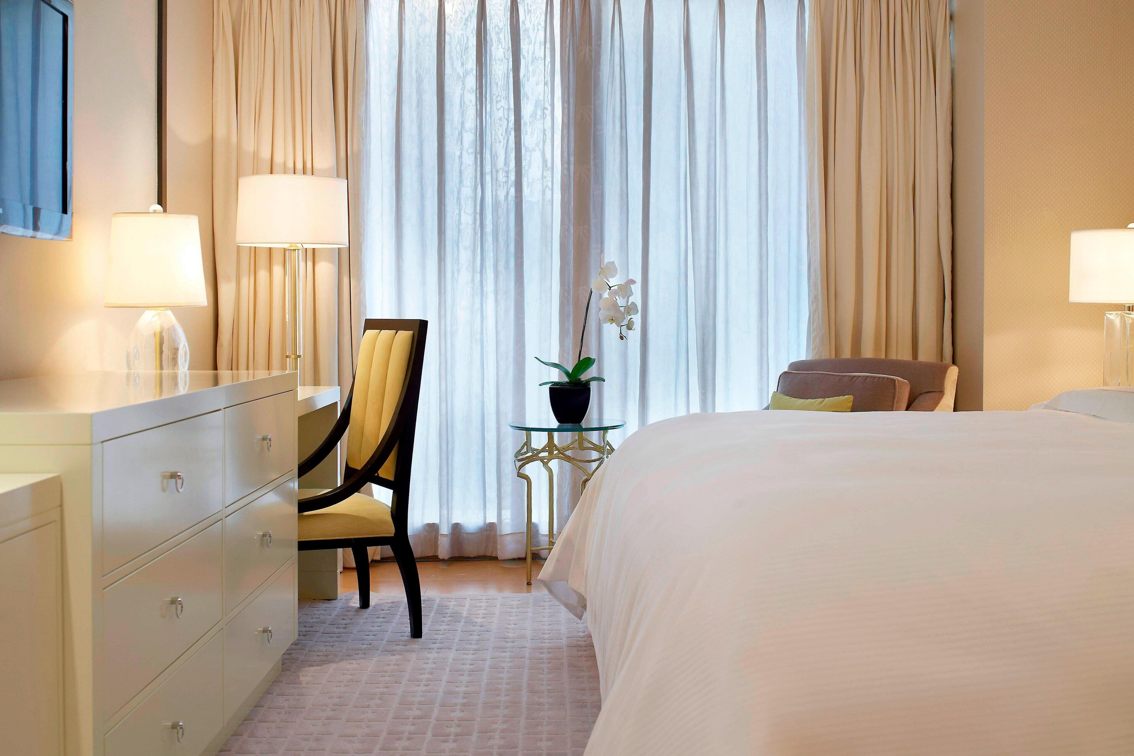 A hotel room with a bed, a chair, a desk, and a dresser.