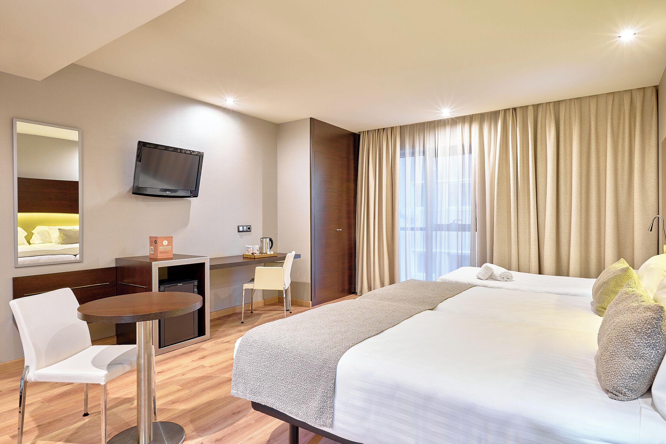 Hotelkamer met een bed, een bureau, een stoel, een televisie en een groot raam met gordijnen.