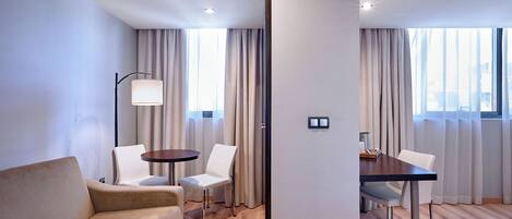 Una habitación de hotel moderna con un sofá, dos sillones, una mesita y una lámpara.