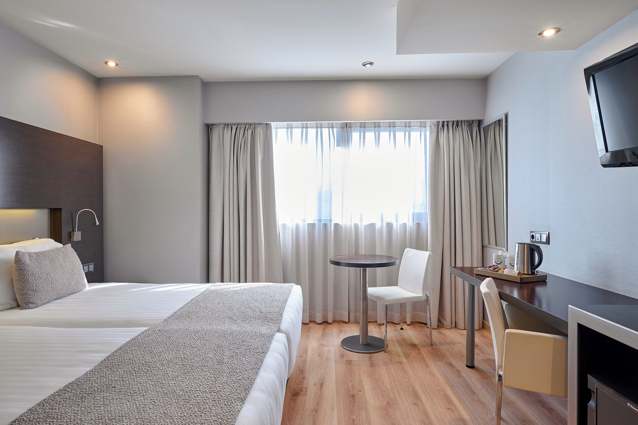 Habitación de hotel con cama, escritorio, silla, televisor y ventana con cortinas.