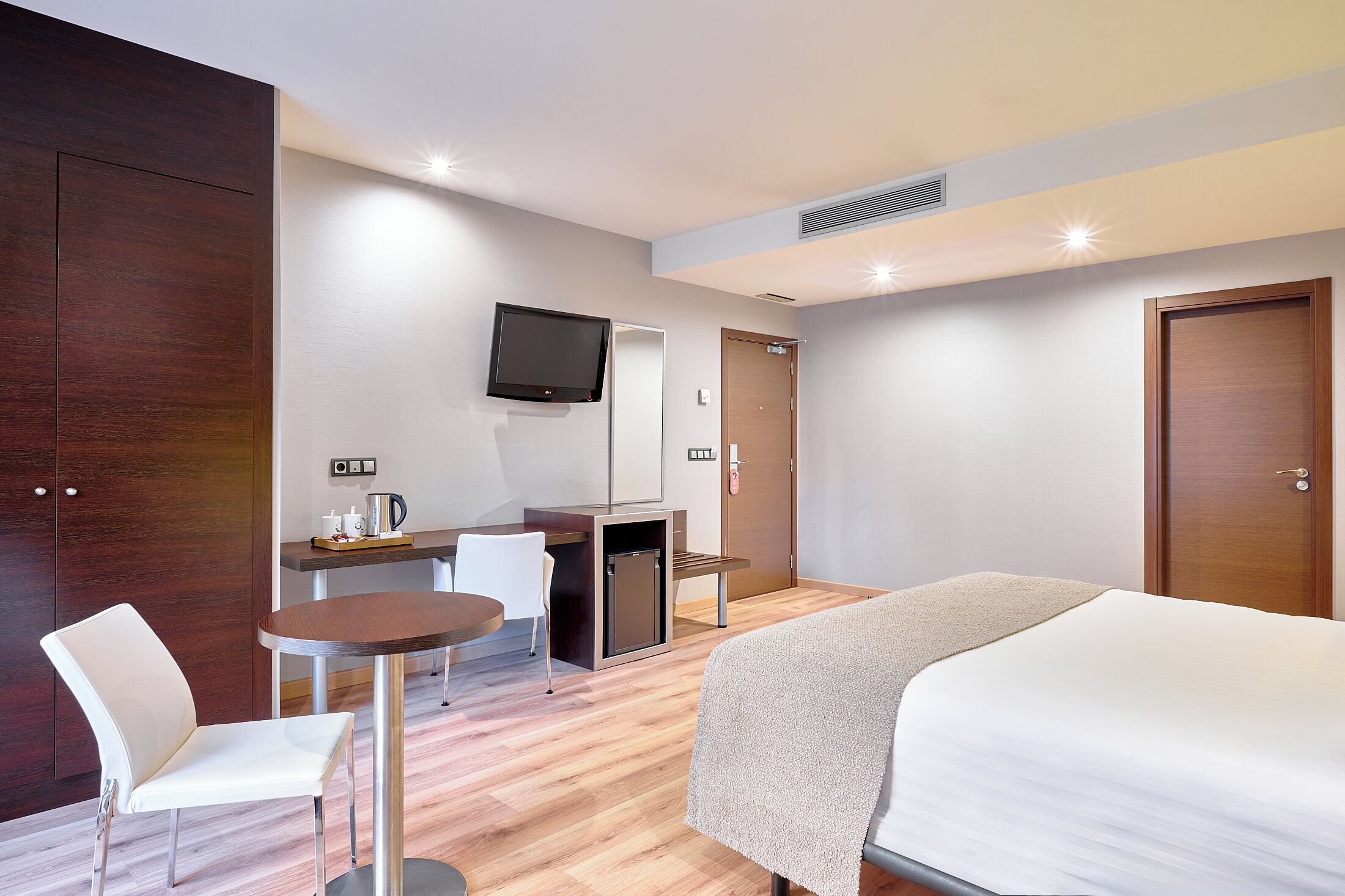 Una habitación de hotel con una cama, un escritorio con una silla, un televisor y una cafetera.