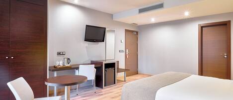 A hotel room with a bed, a desk with a chair, a television, and a coffee machine.