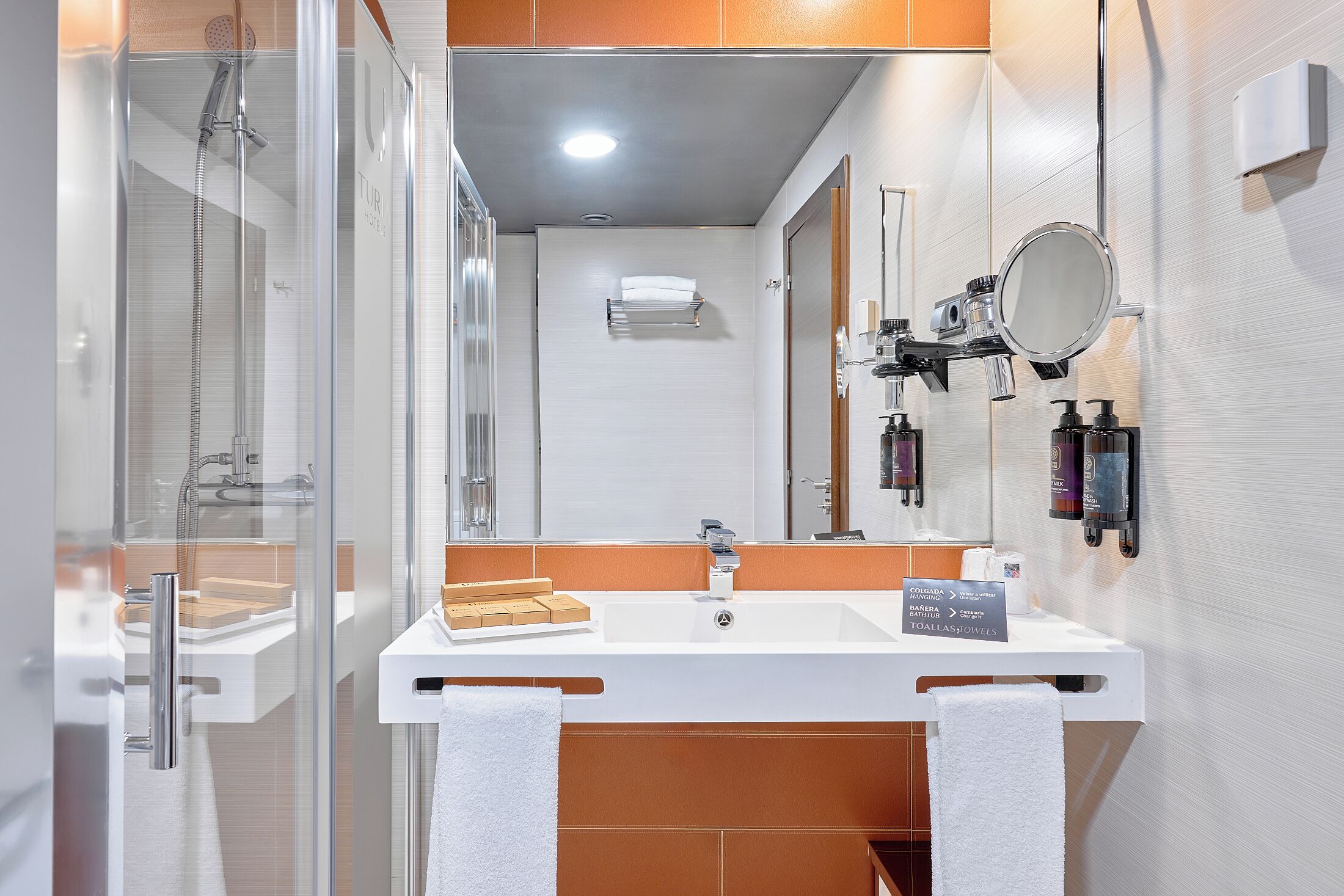 Un baño moderno con ducha de vidrio, un lavamanos blanco con espejo y artículos de tocador en la pared.