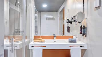 Un baño moderno con ducha de vidrio, un lavamanos blanco con espejo y artículos de tocador en la pared.