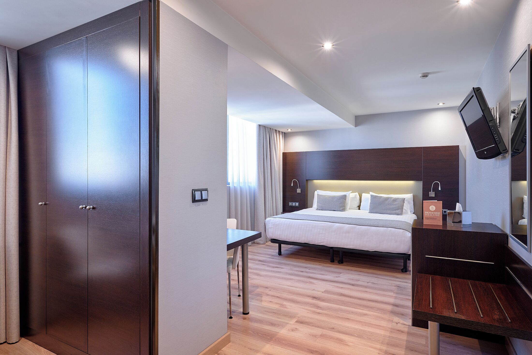 Quarto de hotel moderno com uma cama grande, uma escrivaninha, um guarda-roupa e uma TV de tela plana na parede.
