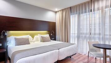 A modern hotel room with a large bed, bedside tables, a chair, and a small table.