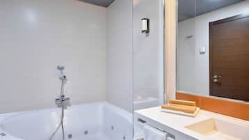 Un baño moderno con una bañera independiente, cabina de ducha con paredes de vidrio y un mueble de tocador blanco con espejo y puerta de madera.