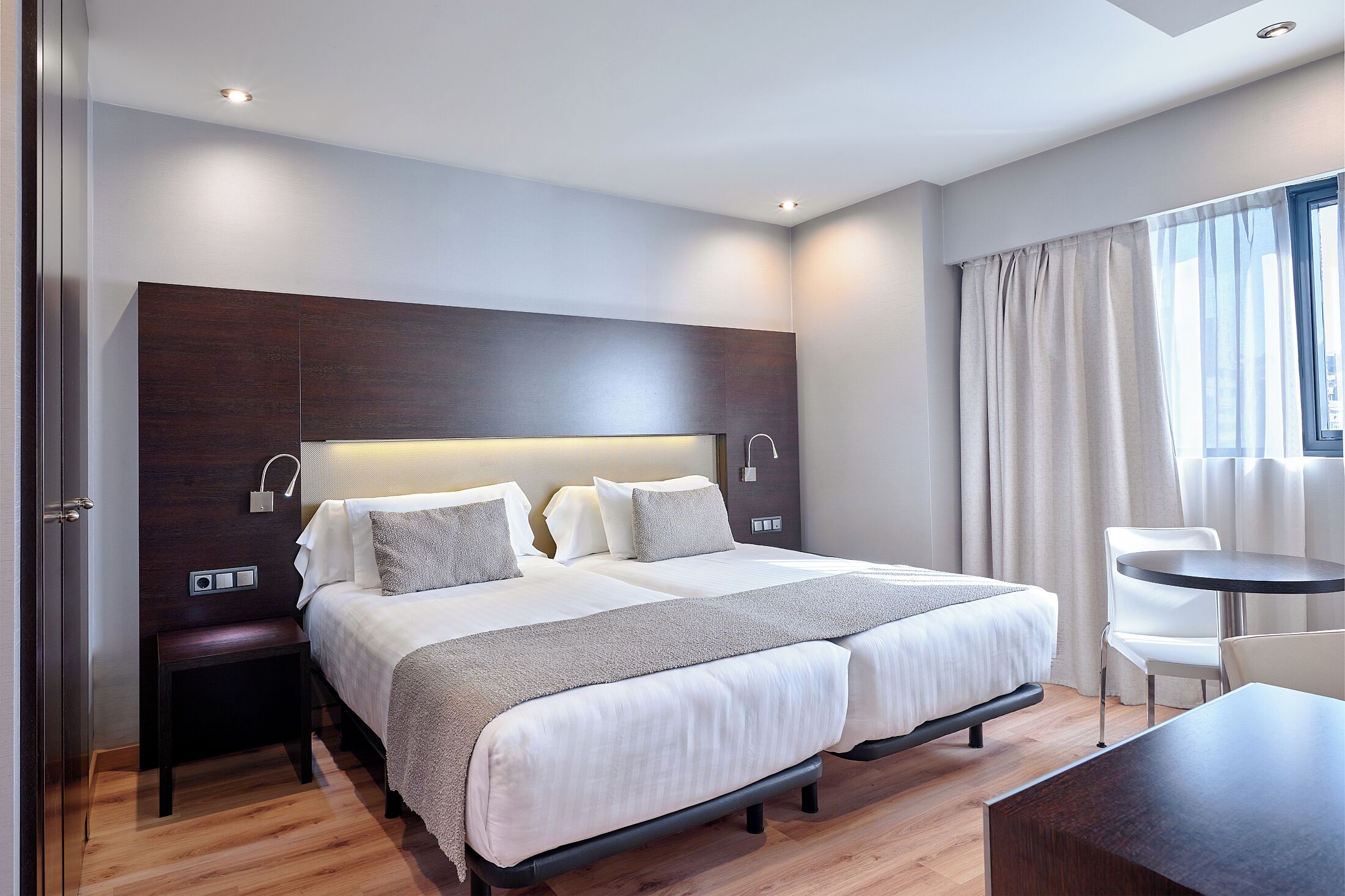 Una habitación de hotel moderna con una cama doble, mesitas de noche, un pequeño escritorio y una silla.