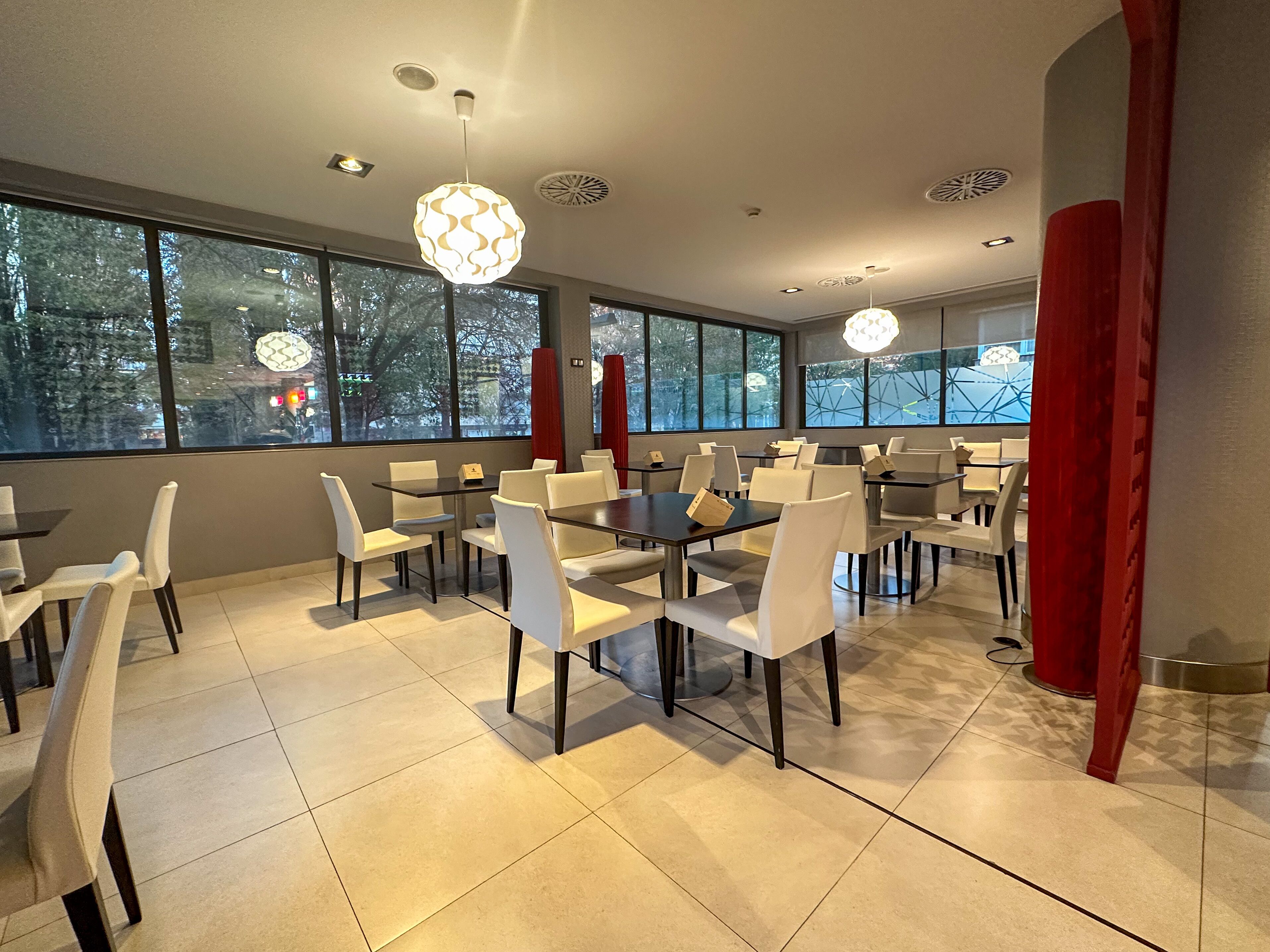 Un comedor moderno con mesas y sillas, ventanas amplias e iluminación decorativa.