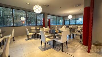 Un comedor moderno con mesas y sillas, ventanas amplias e iluminación decorativa.
