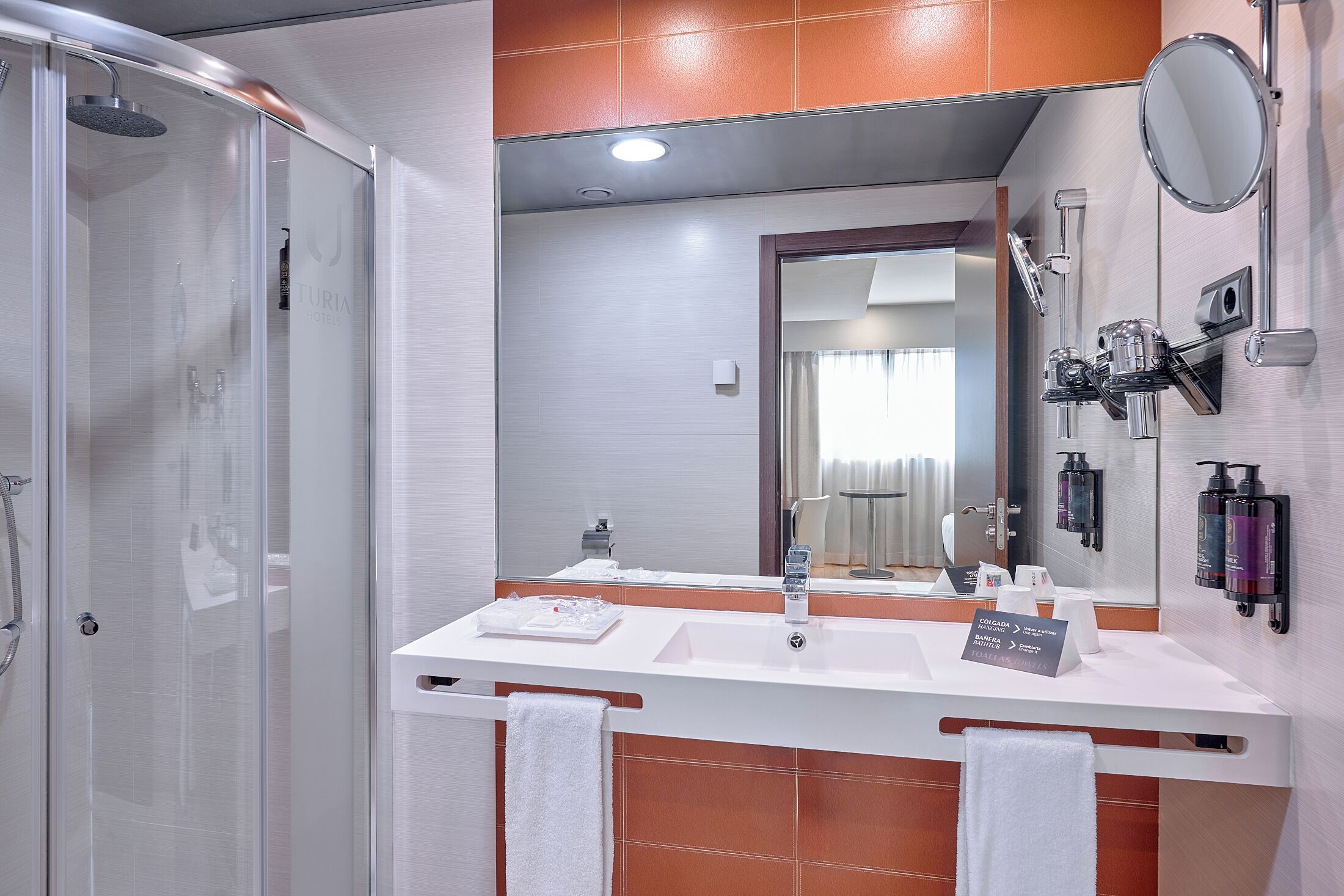 A modern bathroom with a glass-enclosed shower, a white sink, and a large mirror.