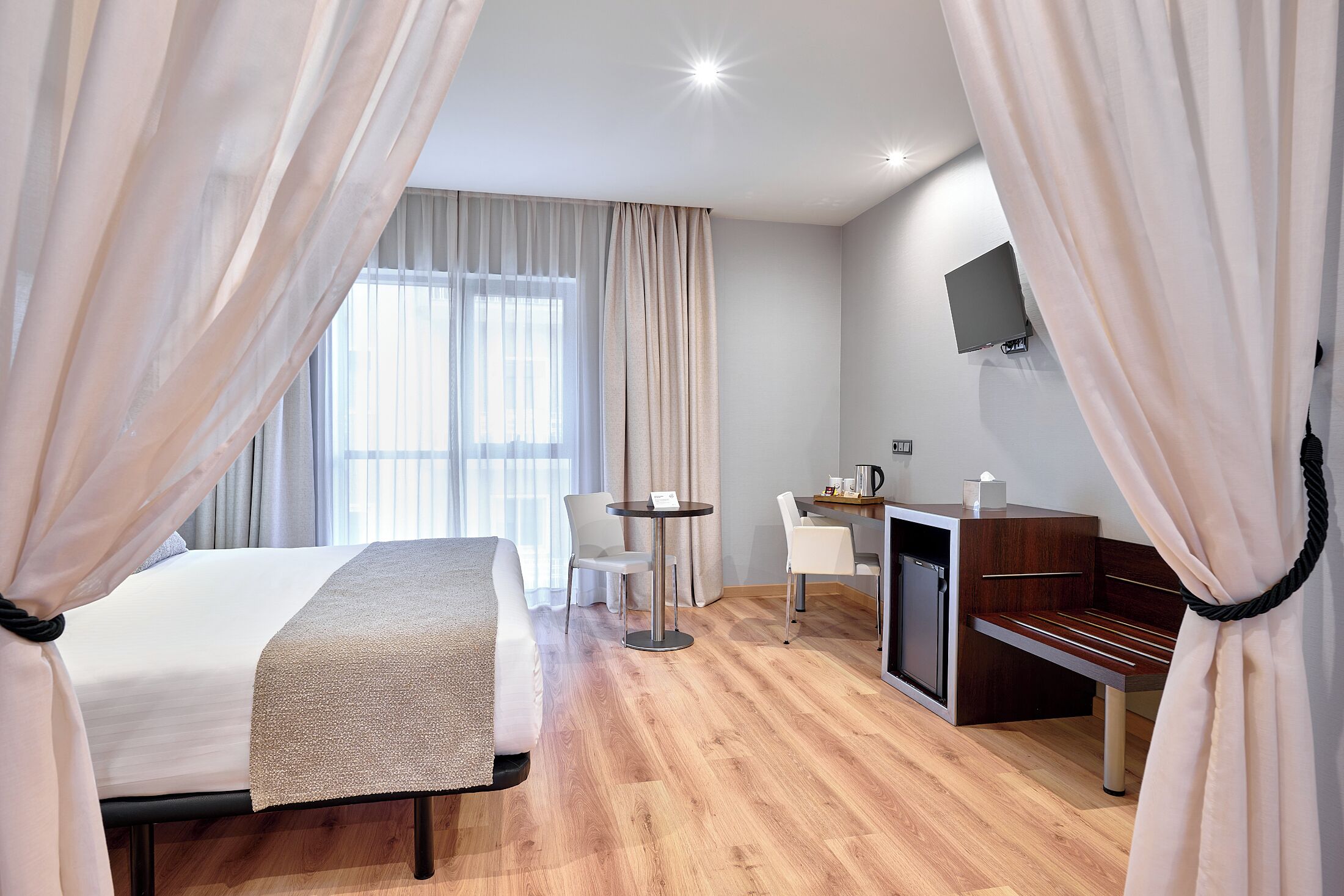 A hotel room with a bed, a desk, a chair, a television, and a window with curtains.
