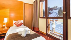 A hotel room with a large window, wooden walls, a bed with white bedding, a red pillow, and a wooden nightstand with a lamp.