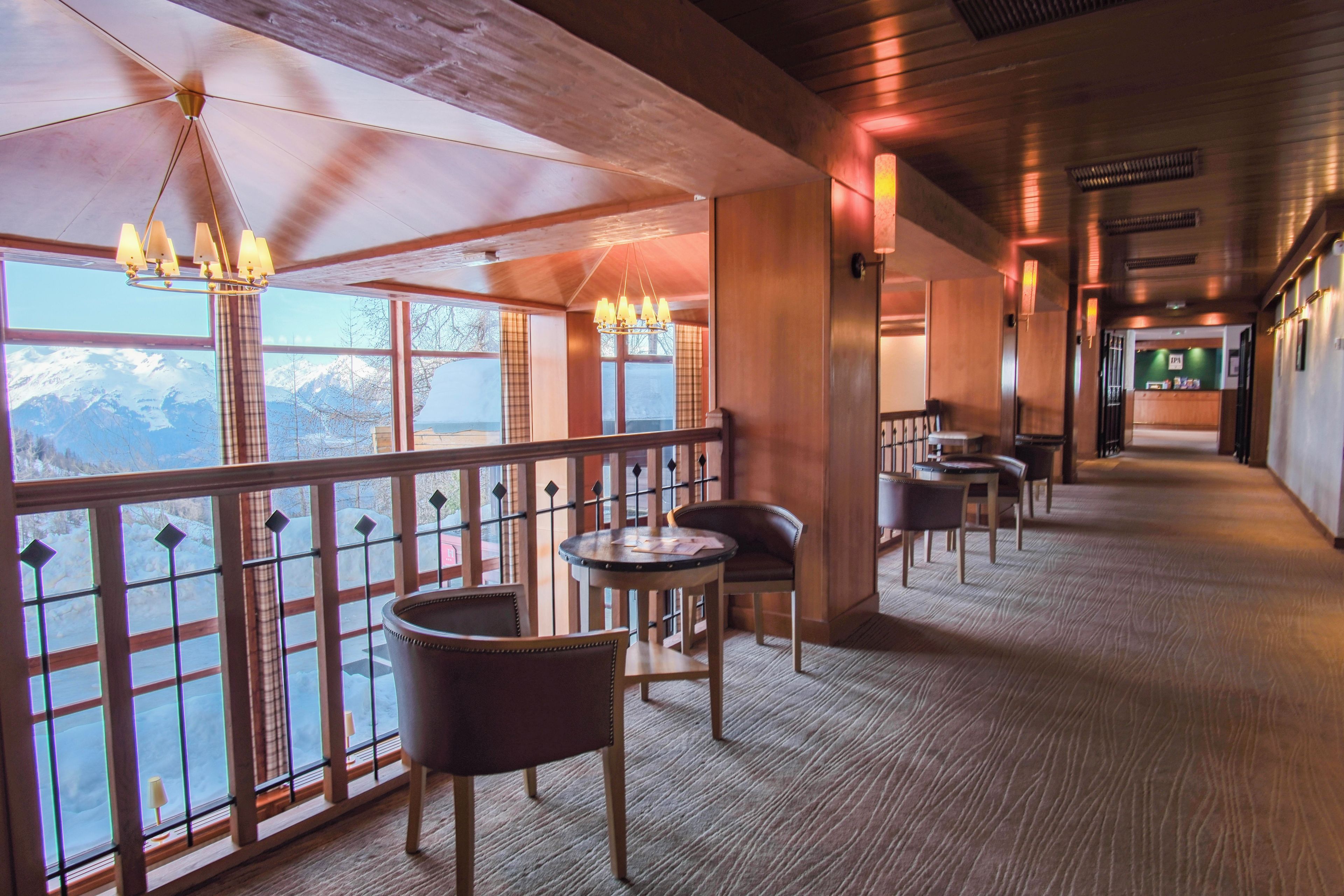 A corridor with a view of mountains, wooden walls, and a seating area with tables and chairs.