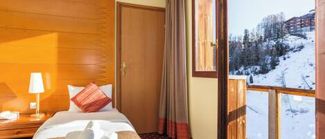 Una camera d'hotel con un letto, un comodino, una lampada e una finestra vista su un paesaggio innevato.