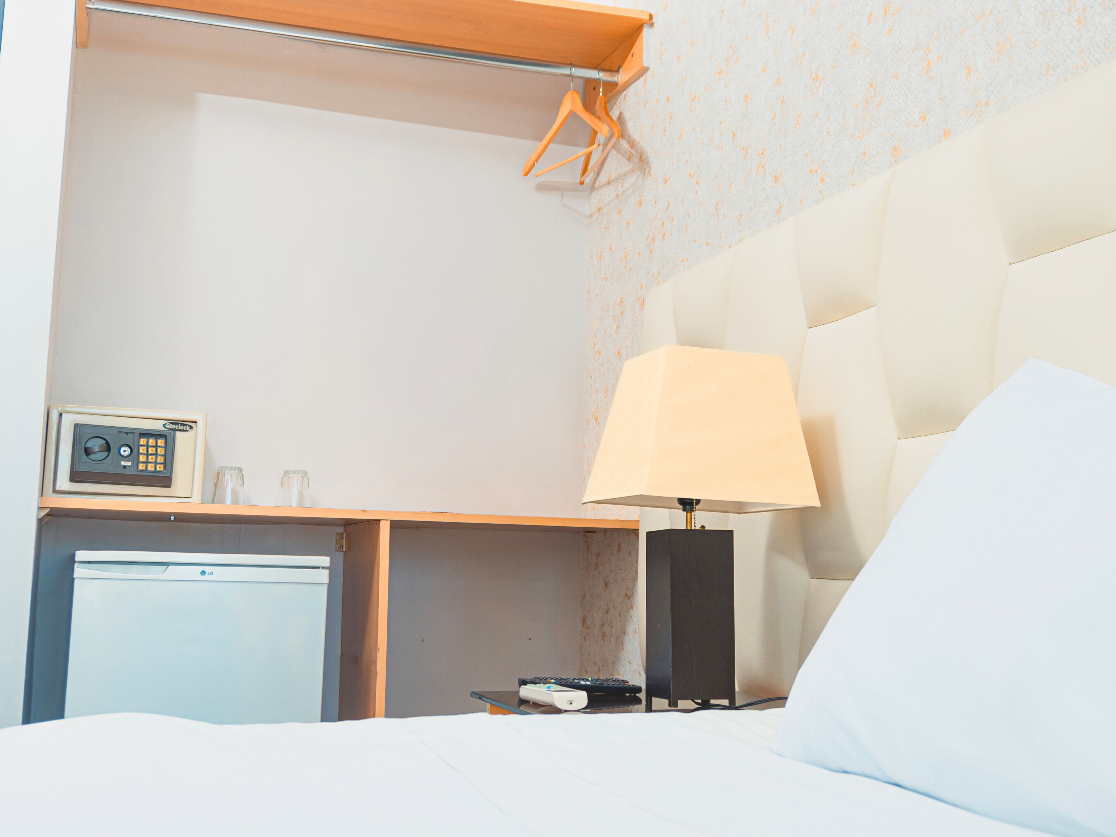 Une chambre d’hôtel équipée d’un lit, d’une table de chevet, d’une lampe, d’une télécommande et d’un petit réfrigérateur.