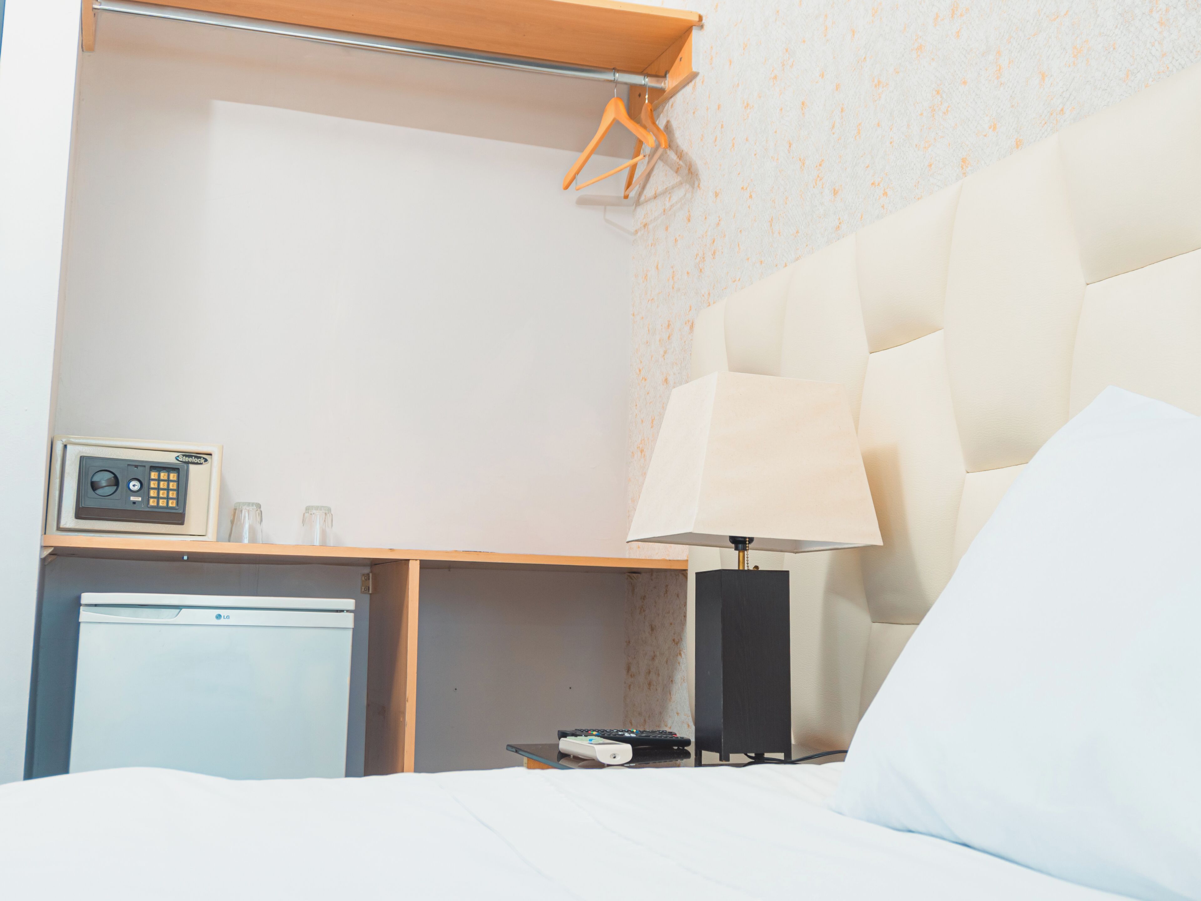 Une chambre d’hôtel avec un lit, une table de chevet avec une lampe, un petit réfrigérateur et une radio fixée au mur.